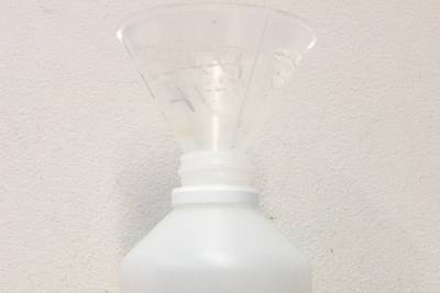 Plastic bottle fitted with a funnel on top and half full of 70% ethanol inside. Orange tape labels the bottle 
